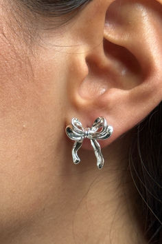 A close-up view of a person's ear wearing a shiny silver bow-shaped earring with a handcrafted, slightly textured finish. The earring adds an elegant and whimsical touch to the look. Trendy Bows, Jewelry Styles, Bow Earrings, Bow Design, New Jewelry, Holiday Looks, Ear Studs, Jewelry Box