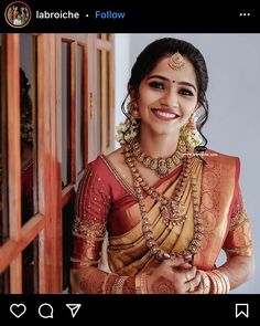 a woman in a red and gold saree smiles for the camera with her hands on her hips