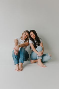 two women are sitting on the floor posing for a photo with their arms around each other