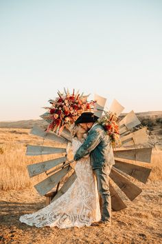 a bride and groom kissing in front of an old wooden windmill as the sun sets