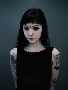 a woman with long black hair and tattoos on her arm, looking at the camera