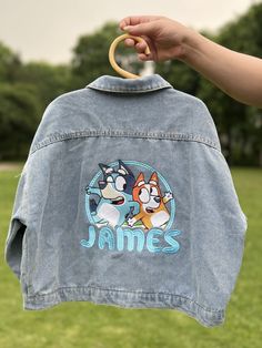 someone holding up a jean jacket with an image of two cartoon characters on the back