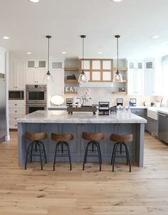 a large kitchen with an island and three stools in it, along with stainless steel appliances