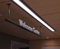 a welcome center sign hanging from the ceiling in an office building with lights on it