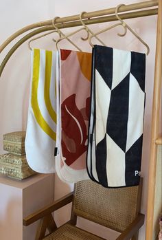 three towels hanging on a clothes rack next to a wooden chair and shelf with books