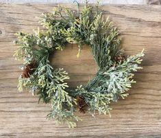 a wreath with pine cones and evergreen needles hanging on a wooden wall or table top