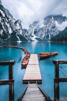 several boats are docked at the end of a pier in front of snow covered mountains