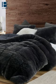 the bed is made with black fur and white pillows on top of wooden flooring