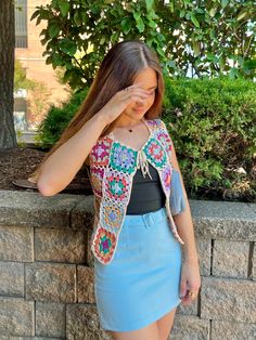 a woman standing next to a brick wall wearing a crocheted vest and skirt