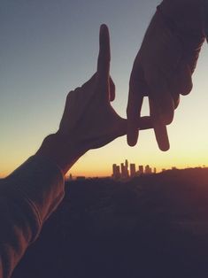 two people holding up their fingers in front of the sun setting over a cityscape