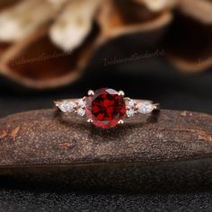 a red and white diamond ring sitting on top of a piece of wood next to some flowers