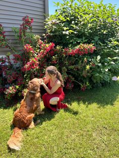 a woman kneeling down next to a dog in front of some bushes and red flowers