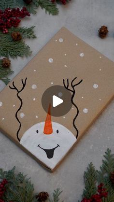 a canvas with a snowman's face painted on it, surrounded by evergreen branches and pine cones