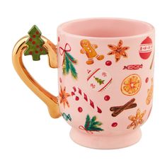 a pink coffee mug with christmas decorations on it and a gold handle is sitting in front of a white background