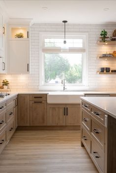 a kitchen with wooden floors and white walls, along with open shelving units on either side of the window