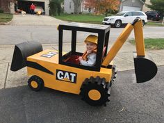 a child in a construction vehicle costume on the street with a toy bulldozer