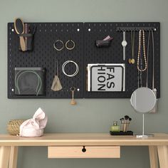 a wall mounted jewelry organizer on a gray wall above a wooden table with a mirror