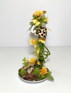 an arrangement of flowers and plants in a vase on a white tablecloth with a black leopard print hat