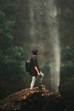 a man standing on top of a rock in front of a waterfall with a backpack