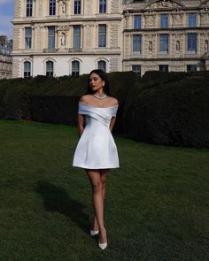 a woman in a short white dress is standing on the grass near a large building