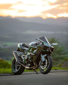 the motorcycle is parked on the side of the road in front of some hills and trees