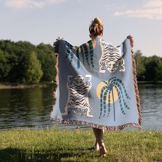 a woman is holding up a towel with palm trees on it in front of a body of water