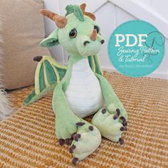 a green stuffed dragon sitting on top of a brown floor next to a white pillow