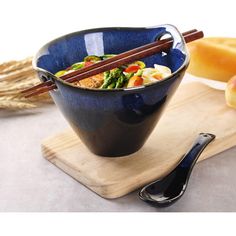 a blue bowl with chopsticks in it on a wooden board next to bread