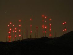 many red lights are lit up in the night sky over a hill with hills and trees