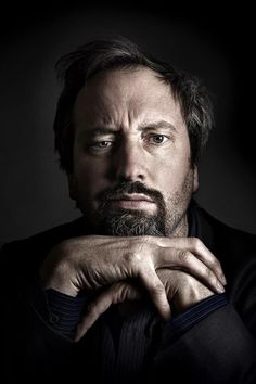 a man with a beard and black shirt posing for a photo in front of a dark background