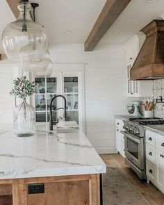 a kitchen with white cabinets and marble counter tops, an island in front of the stove