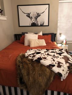 a bed with a cow print on the wall above it and an orange bedspread