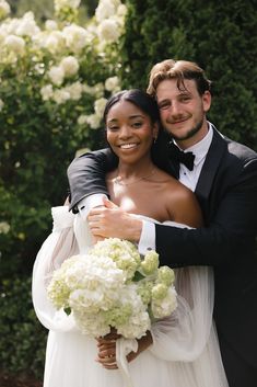 a bride and groom hugging each other in front of white flowers