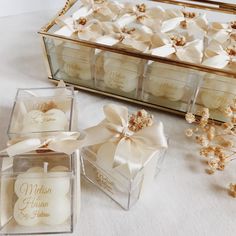 two glass boxes filled with white candles and some flowers next to each other on a table