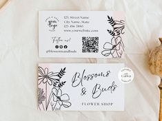 two business cards sitting next to each other on top of a white sheet with flowers