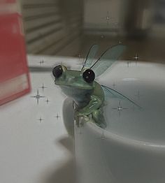 a green frog sitting on top of a white cup