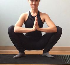 a woman sitting on a yoga mat with her hands in the air and looking at the camera