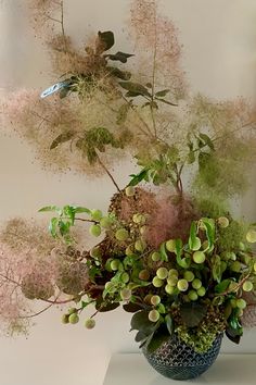 a vase filled with lots of green and pink flowers on top of a white table