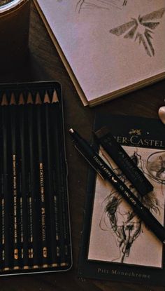 a wooden table topped with lots of pencils next to a drawing book and cup of coffee