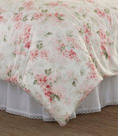 a bed with pink flowers on it and white ruffled bedspread over the top