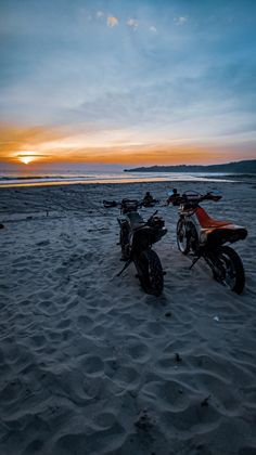 two motorcycles parked on the beach at sunset