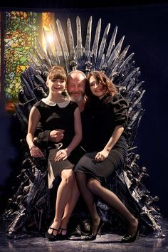 three people sitting on the iron throne with their arms around each other