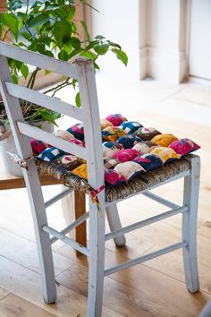 a white chair with a colorful cushion on it's seat and a potted plant in the back