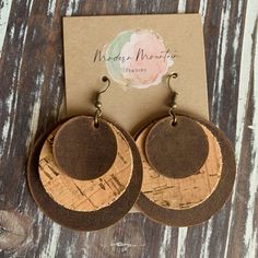 the cork earrings are made from wood and have brown leather circles with gold accents on them