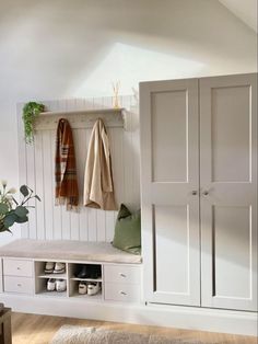 a white coat rack with two coats hanging on it's sides and some shoes