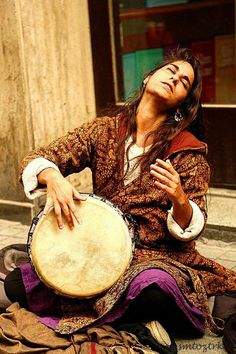 a woman sitting on the ground playing a drum