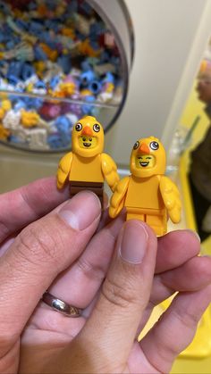 two small yellow toy birds sitting on top of someone's hand in front of a pile of toys