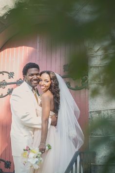 a bride and groom pose for a photo in front of a red door at their wedding