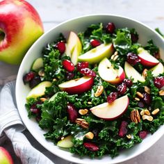 an apple and kale salad with cranberries in a white bowl on a table