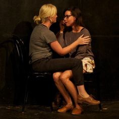 two women sitting on a chair with their arms around each other as they look at each other